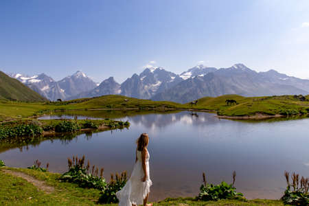 A woman in a white dress at the Koruldi Lake with a dream like view on mountains near Mestia in the Greater Caucasus Mountain Range,Upper Svaneti,Country of Georgia.Horses at the water shore.Wedding.の写真素材