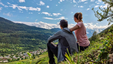 A couple enjoying the amazing view on the valley in Mestia in the Greater Caucasus Mountain Range, Upper Svaneti, Country of Georgia. Clouds cover the snow capped mountain peaks.Outdoor,Trekkingの写真素材