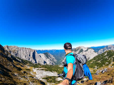 Man with backpack filming himself while hiking to the summit of Hinterer Polster in the scenic region of the Hochschwab mountain in Styria, Austria. Alpine meadows and sharp rocks. Hike concept. Freeの写真素材