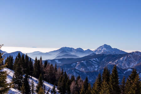 Panoramic view on snow capped mountain peaks of Karawanks in Carinthia, Austria. Julian Alps. Winter wonderland in the Austrian Alps, Europe. Ski tour, snow shoe hiking. Hochobir. Blue misty hills.の写真素材