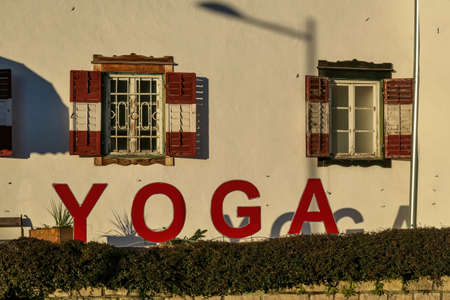 A yoga house in the village of Poertschach at the Woerthersee in Carinthia, Austria. The sun is hitting the walls of the house. The window blinders are open. Big yoga sign in front of the buildingの写真素材