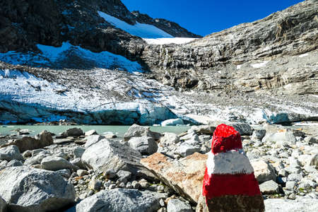 Red white path mark with scenic view on a glacier lake near Hoher Sonnblick in the mountains of High Tauern Alps in Carinthia, Salzburg, Austria, Europe. Goldbergkees in Hohe Tauern National Parkの写真素材