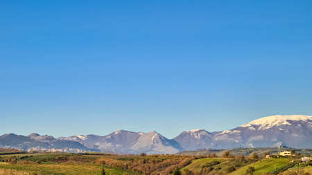 Panoramic view on small rural villages on yellow hill on the countryside in Calabria, Italy Europe. Snow capped mountains in the back. Apennine Mountains on a clear and sunny dayの写真素材