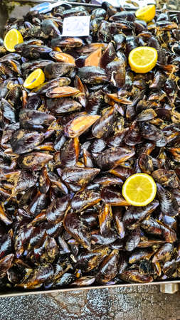 Close up view on a table full of fresh mussels with lemon on daily fish market in Catania, Sicily, Italy, Europe. Stall with local types of fresh seafood. La Pescheria. Traditional bazaarの写真素材