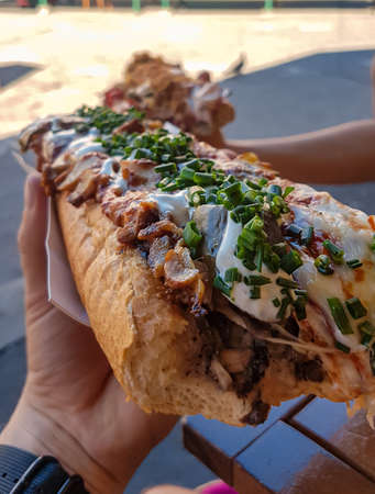 A massive grilled bread roll topped with various ingredients, like pickles, pickled pepper, fried...