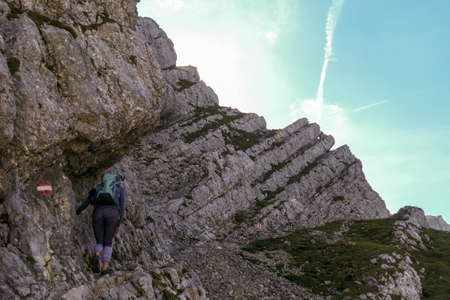 A woman with backpack hiking through steep and high mountain crater in Austrian Alp. The sun shines...