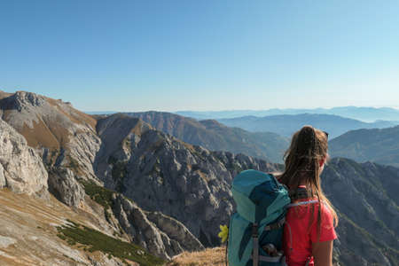 A woman with big blue backpack enjoying the view on valley from top of a mountain in Hochschwab region in Austrian Alps. The flora overgrowing the slopes is turning golden. Freedom. She is happyの写真素材