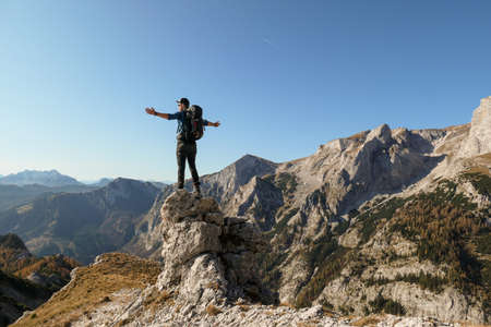 A man standing on top of a sharp, pointy boulder in Hochschwab region, Austrian Alps. The steep mountain wall in front look very dangerous. High mountaineering. Autumn vibes. Adventure and freedomの写真素材
