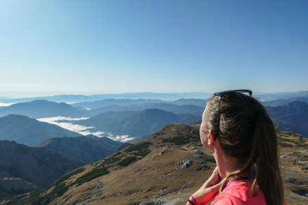 A woman enjoying the view on valley shrouded in fog from top of a mountain in Hochschwab region in Austrian Alps. The flora overgrowing the slopes is turning golden. Freedom. Mysterious landscapeの写真素材