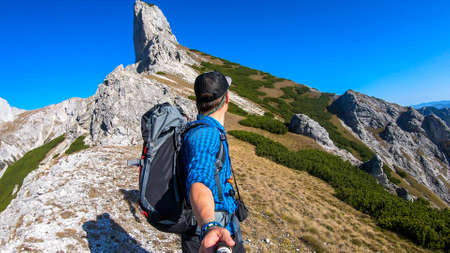 A man hiking in Hochschwab region in Austrian Alps. He is planing to climb a sharp rock. He is taking a selfie. Idyllic landscape. Freedom and wilderness. Pathless wandering. Massive mountain chainの写真素材