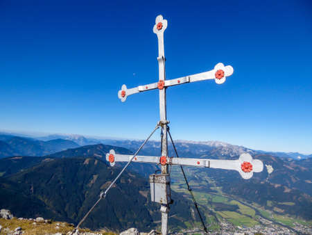 A cross on top of Kaiserau Kreuzkogel, Austrian Alps. The cross has transverse arms. Behind it there is a panoramic view on the whole region. Clear and bright day. Achievementの写真素材