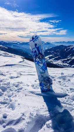 A snowboarding board sticked into a pile of fresh snow on top of Katschberg in Austria. Panoramic view on the surrounding mountains. Winter wonderland, Clear and sunny winter day.の写真素材