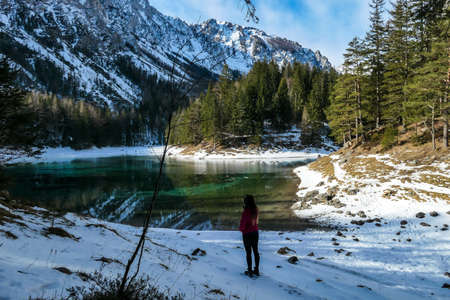 A woman walking to the shore of Green Lake in Austrian Alps. Mountains and ground are covered with...