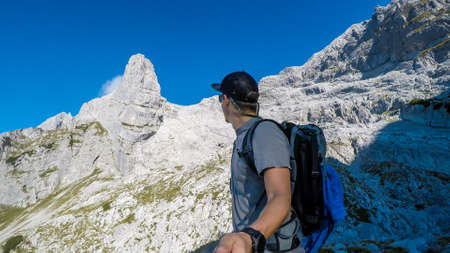A man taking a selfie while hiking in stony Alpine region in Austria. The sky is blue, with one...