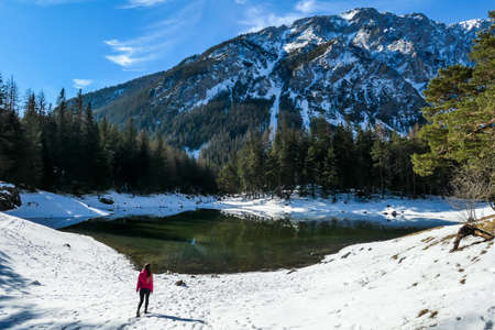 A woman standing at the stone next to the shore of Green Lake in Austrian Alps. Mountains and ground...