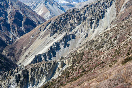 A close up view on a valley along Annapurna Circuit in Nepal. In the back there are high, snow capped Himalayan peaks. Slopes are overgrown with small bushes. Exploration and discovering new placesの写真素材