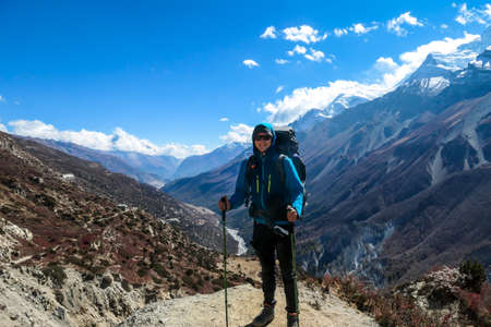 A man enjoying her trek to Tilicho Lake, along Annapurna Circuit in Nepal. In the back there are high, snow capped Himalayan peaks. Slopes are overgrown with small bushes. Exploration and discoveringの写真素材