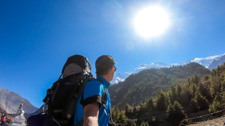 A man taking a selfie while trekking along Annapurna Circuit in Nepal. He is enjoying the view and trek. There is a lush green Himalayan valley around him. Snow caped mountains in the backの写真素材