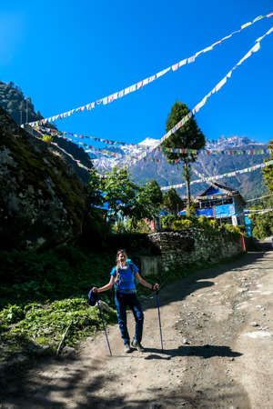 A woman in hiking outfit standing in front of a small Himalayan village. Colorful prayer flags waving above the Himalayan peaks along Annapurna Circuit Trek, Nepal. Meditation and peace of mind.の写真素材