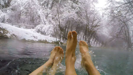 Two pairs of feet soaking in a natural thermic spring in Maibachl, Austria during snowfall, winter. The thermic pool is located in the middle of the forest. Healing power of natural water. Relaxationの写真素材