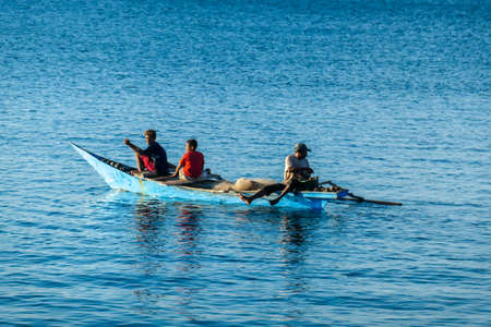 Flores/Indonesia 20290808: A fishermen's boat crossing a calm sea near Maumere, Indonesia There are three men in one small, blue boat, one of them is paddling. Calm surface of the sea.の写真素材