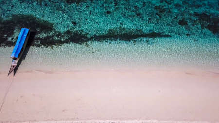 A drone shot of a boat anchored to pink sand beach on a small island near Maumere, Indonesia. Happy and careless moments. Waves washing the shore. Clear, turquoise coloured water displaying coral reefの写真素材