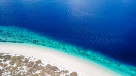A drone shot of a pink sand beach on a small island near Maumere, Indonesia. Happy and careless moments. Waves gently washing the shore.Clear, turquoise coloured water displaying coral reef.の写真素材