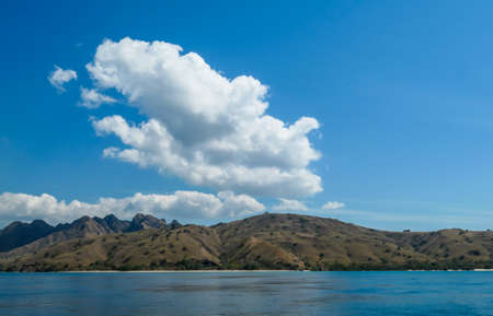 A view on idyllic island in Komodo National Park, Indonesia. There are few clouds above the island. Calm and clear surface of the sea. Island hoping. Perfect day for sailingの写真素材