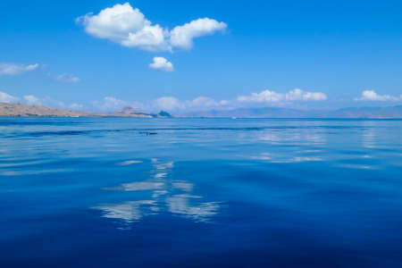 Calm surface of the sea reflecting the sky in Komodo National Park, Indonesia. The sea surface is almost exact copy of the sky. There is an island in the back. Heart shaped cloud.の写真素材