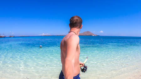 A man holding a snorkelling masker, walking on a shallow sea water while taking selfies in Komodo National Park, Indonesia. He is enjoying the moment, having fun while island hopping.の写真素材
