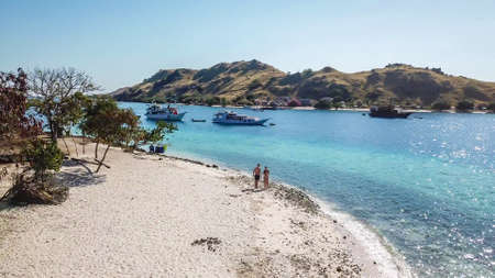A drone shot of a couple walking on a white sand beach in Komodo National Park, Flores, Indonesia....