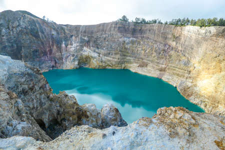 Close up view on the Kelimutu volcanic crater lakes in Flores Indonesia. Lakes are shining with many shades of turquoise and blue. Sun shines through clouds. Barren and sharp slopes of volcanic craterの写真素材