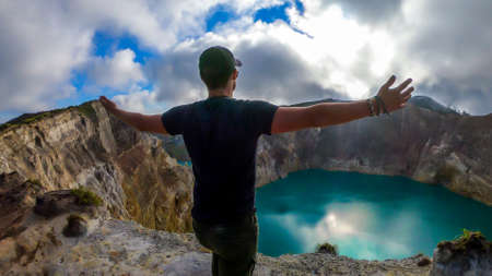 Man standing at the volcano rim with arms spread and watching the Kelimutu volcanic crater lakes in Moni, Flores, Indonesia. Man engages with life and has the feeling of freedomの写真素材