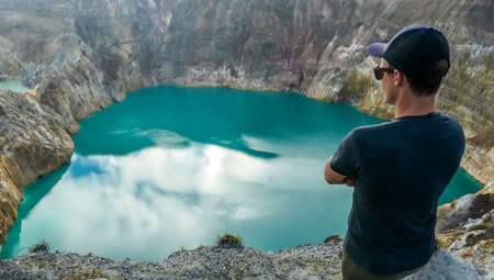 Man standing at the volcano rim and watching the Kelimutu volcanic crater lakes in Moni, Flores, Indonesia. Man engages with life and has the feeling of freedomの写真素材