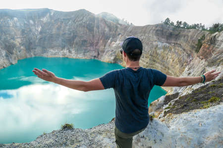 Man standing at the volcano rim with arms spread and watching the Kelimutu volcanic crater lakes in Moni, Flores, Indonesia. Man engages with life and has the feeling of freedomの写真素材