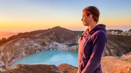 A woman watching the sunrise over the Kelimutu volcanic crater lakes in Moni, Flores, Indonesia. Woman is relaxed and calm, enjoying the view on turquoise lake. Golden hour over the volcanoの写真素材