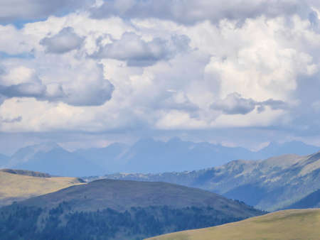 Hiking trails in the high mountain. Green grass and bushes cover the slopes. Endless chains of mountains visible. Thick clouds on the sky. Solo walk allowing for reverie and reflection. Natural beautyの写真素材