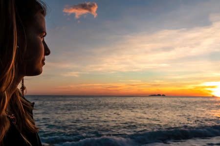 Happy woman enjoying sunset from Marina Grande beach in Positano at Amalfi Coast, Italy, Campania, Europe. Selective focus on person face. Sun going down behind Li Galli islands in Mediterranean Seaの写真素材
