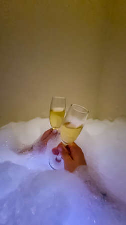 Couple toasting with champagne on honeymoon in a warm bubble bath in a relaxed atmosphere in bathroom. Relaxing in bath drinking prosecco. Love, relationship concept. Vacation in luxury hotelの写真素材