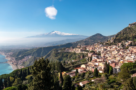 Panoramic view on snow capped Mount Etna volcano and Mediterranean coastline on sunny day seen from coastal hilltop town Taormina, island Sicily, Italy, Europe, EU. Vacation tourism travel destinationの写真素材