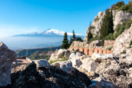 Panoramic view of snow capped Mount Etna volcano on a sunny day seen from the ancient Greek theater of Taormina, island Sicily, Italy, Europe, EU. Selective focus on walls of the archeological ruinsの写真素材