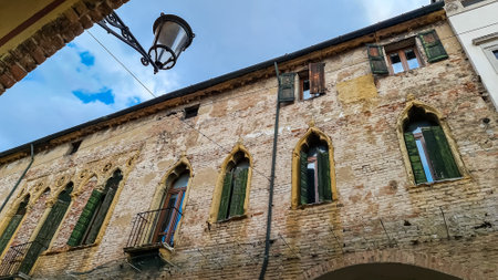 A bottom up scenic street view the historic city center of Padua, Veneto, Italy, Europe. Facade of the building are old and rustic. The window blinders are green and made of wood. Sunny day in summerの写真素材