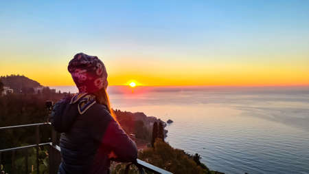 Tourist woman with scenic view on beautiful landscape at sunrise at Mediterranean Ionian sea seen from the main square (Piazza IX Aprile) in Taormina, Province of Messina, Sicily, Italy, Europe, EUの写真素材