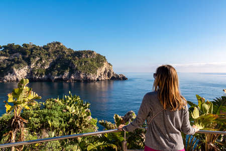 Woman enjoying a scenic view on sunny day from touristic paradise island Isola Bella in Taormina,...