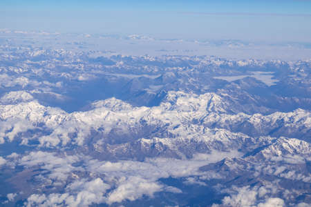 Window view from an airplane on the snow capped mountain ranges of the Alps at the border Austria...
