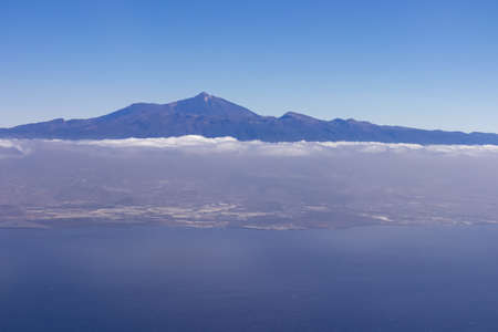 Window view from an airplane on the volcano mountain peak of Pico del Teide on Tenerife, Canary Islands, Spain, Europe, EU. High peak are shrouded in clouds. Flying high above the ground. Freedomの写真素材