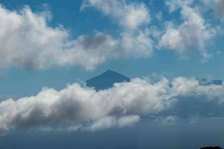 Scenic view on the cloud covered volcano mountain peak Pico del Teide on Tenerife seen from La Gomera, Canary Islands, Spain, Europe. Mystical magical atmosphere on hiking trail to Roque de Agandoの写真素材