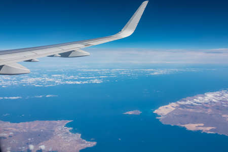 Aerial window view from an airplane on Fuerteventura and Lanzarote, Canary Islands, Spain, Europe, EU. Wing and turbines of the aircraft can be seen. Flying high above the ground. Freedom. Flyingの写真素材