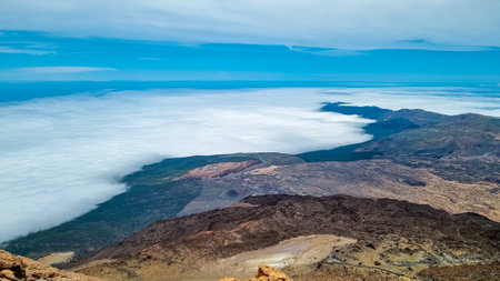 Scenic view from summit of volcano Pico del Teide over the island of Tenerife, Canary Islands, Spain, Europe. Vista on barren landscape, solidified lava, ash, pumice. Valley and sea covered in cloudsの写真素材