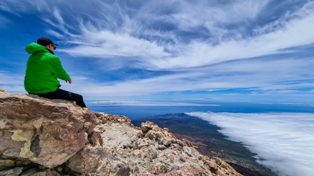 Rear view on hiking man sitting on rock enjoying panorama from summit of volcano Pico del Teide on...